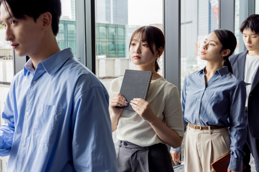 イベントの受付で行列に並ばされ、待ち時間に少し疲れた表情を見せるビジネスパーソン